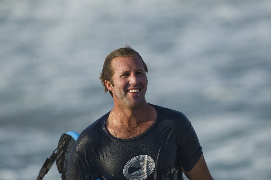 Brent, founder and host, standing with a surfboard in front of Taiwan's coastal mountains